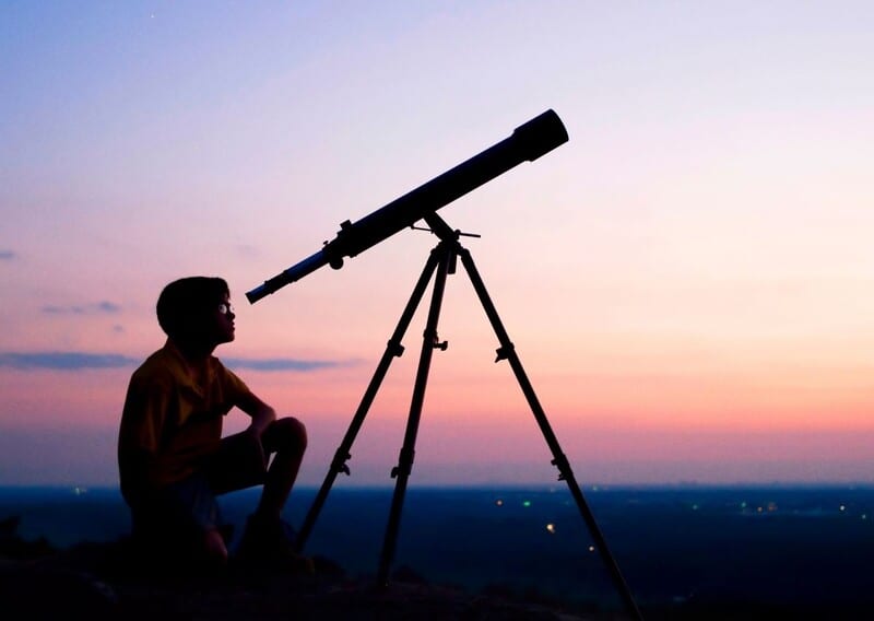 Child at dusk using a telescope